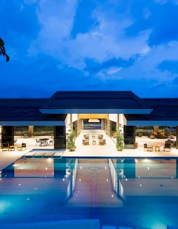 A luxurious building with an illuminated swimming pool outside, set against a vibrant evening sky.