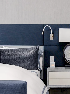 A modern bedroom with a blue and white color scheme, featuring a bed, nightstand, lamp, and decorative pillow.