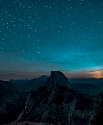 A starry night sky over mountainous terrain with a glowing horizon, creating a serene and breathtaking natural landscape.