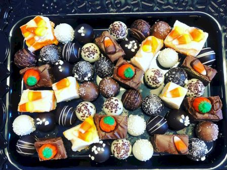 An assortment of chocolates and sweets on a decorative tray, featuring various shapes and toppings like nuts and fruits, in vibrant colors.