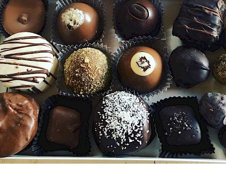 A box of assorted chocolates in various shapes and decorations, neatly arranged in a white box with a gold label on the lid.
