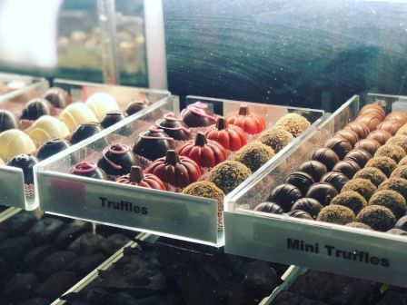 The image shows a display of assorted truffles and mini truffles neatly arranged in trays within a glass case.
