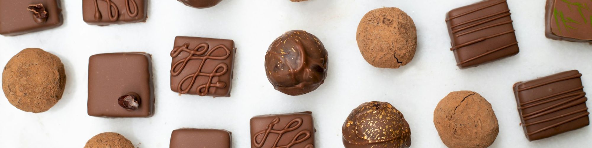 An assortment of chocolates and truffles, featuring various shapes and decorative patterns, arranged on a light surface.