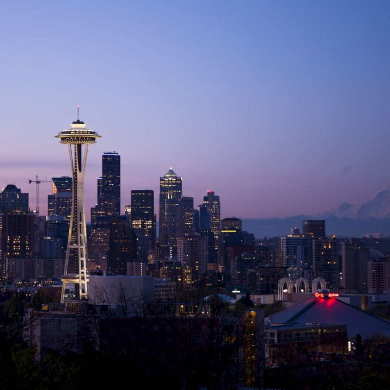 Seattle skyline at dusk with the Space Needle and Mount Rainier in the background, lit by city lights against a twilight sky.