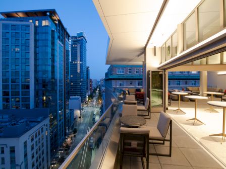 A modern rooftop patio with seating overlooks a city street lined with tall buildings during twilight.
