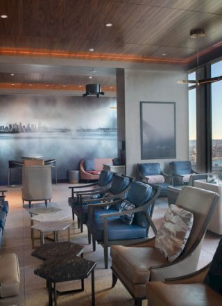 A modern lounge with plush seating, large windows offering a view of the water and a Ferris wheel, featuring a sleek city-themed mural.