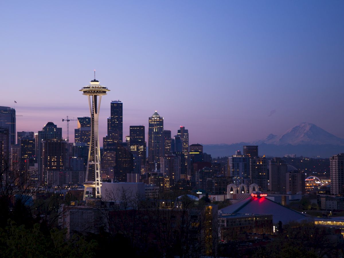 Seattle skyline at twilight featuring the Space Needle, with Mount Rainier visible in the background under a clear sky.
