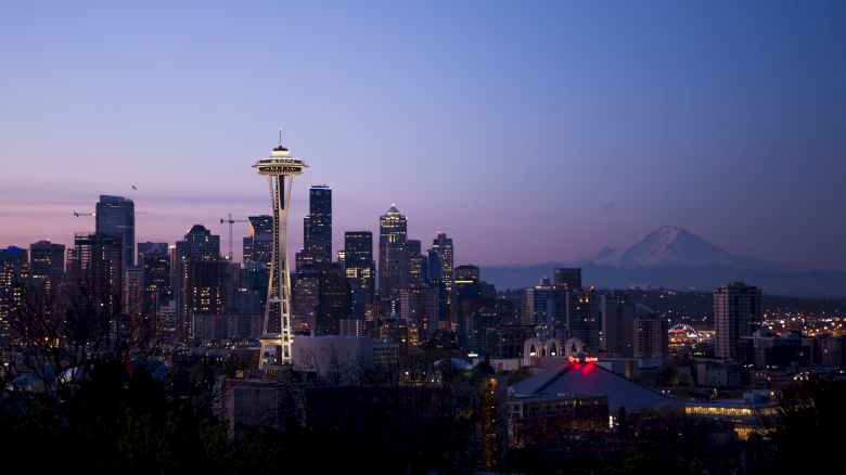 Seattle skyline at twilight featuring the Space Needle, with Mount Rainier visible in the background under a clear sky.